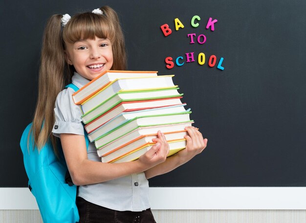 Koncepcja powrotu do szkoły Słodki uczeń z książkami na czarnej tablicy w klasie