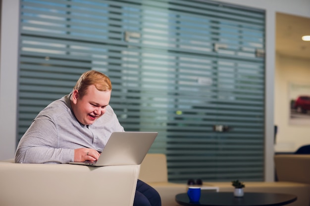 Koncepcja pracy biura. Mężczyzna przegląda laptopa, siedząc w biurze na wygodnej białej kanapie