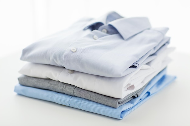 koncepcja prasowania, prania, ubrań, sprzątania i przedmiotów - zbliżenie wyprasowanych i złożonych koszul na stole w domu
