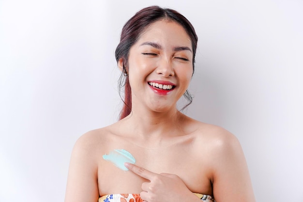 Koncepcja produktów do pielęgnacji skóry Azjatycka kobieta stosująca balsam nawilżający na ciele po prysznicu stojąca owinięta ręcznikiem przycięty obraz
