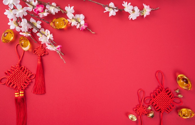 Koncepcja projektu chińskiego nowego roku księżycowego - piękny chiński węzeł z kwiatem śliwki na białym tle na czerwonym tle, leżał płasko, widok z góry, układ napowietrzny.