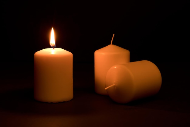 koncepcja przerw w zasilaniu, trzy świece, jedna z płomieniem i dwie rezerwy, na biurku, ciemne tło