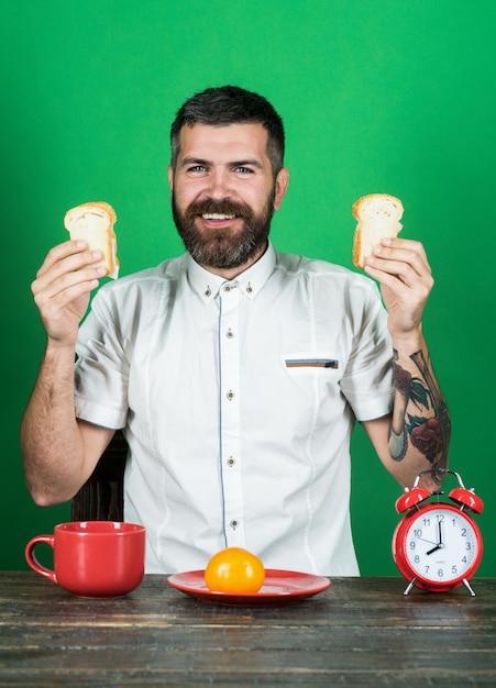 Koncepcja przerwy śniadaniowej lub obiadowej uśmiechnięty brodaty mężczyzna siedzący przy stole trzyma tosty w rękach