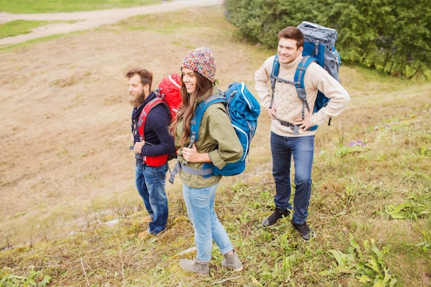 Zdjęcie koncepcja przygód, podróży, turystyki, wędrówek i ludzi - grupa uśmiechniętych przyjaciół z plecakami na zewnątrz