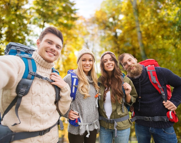 koncepcja przygód, podróży, turystyki, wędrówek i ludzi - grupa uśmiechniętych przyjaciół z plecakami robi selfie na naturalnym tle