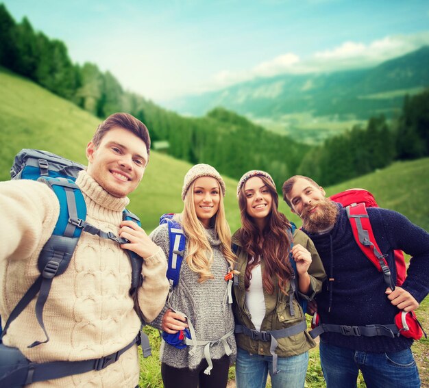 Zdjęcie koncepcja przygód, podróży, turystyki, wędrówek i ludzi - grupa uśmiechniętych przyjaciół z plecakami robi selfie na tle alpejskich wzgórz