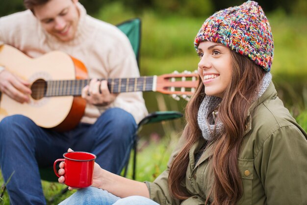 koncepcja przygody, podróży, turystyki i ludzi - uśmiechnięta para z gitarą na kempingu