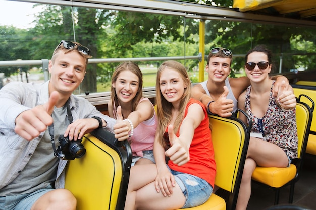 koncepcja przyjaźni, podróży, wakacji, lata i ludzi - grupa szczęśliwych przyjaciół z aparatem cyfrowym podróżująca autobusem wycieczkowym i pokazująca kciuk w górę