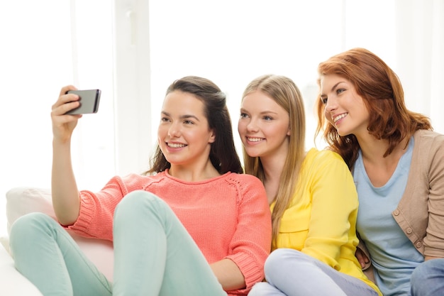 koncepcja przyjaźni, technologii i internetu - trzy uśmiechnięte nastolatki robiące zdjęcie aparatem smartfona w domu