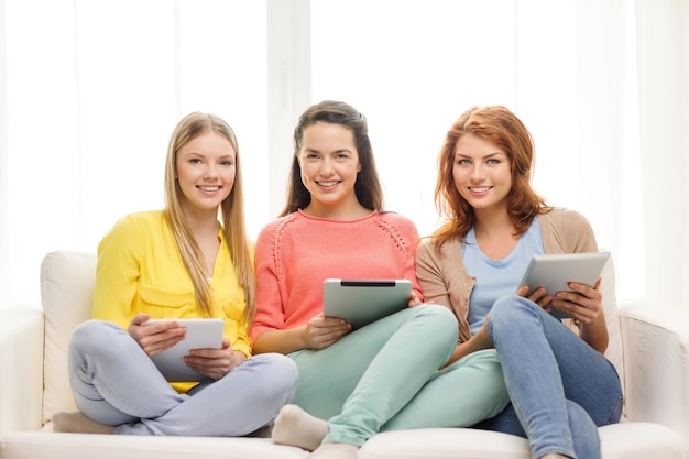 koncepcja przyjaźni, technologii i internetu - trzy uśmiechnięte nastolatki z komputerami typu tablet w domu