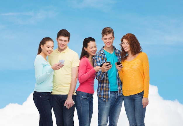 koncepcja przyjaźni, technologii i ludzi - grupa uśmiechniętych nastolatków ze smartfonami nad błękitnym niebem na białym tle chmur