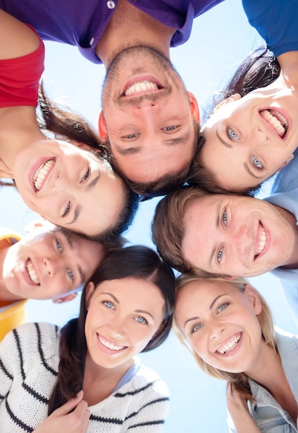 koncepcja przyjaźni, wakacji, wakacji i ludzi - grupa uśmiechniętych przyjaciół stojących w kręgu nad błękitnym niebem