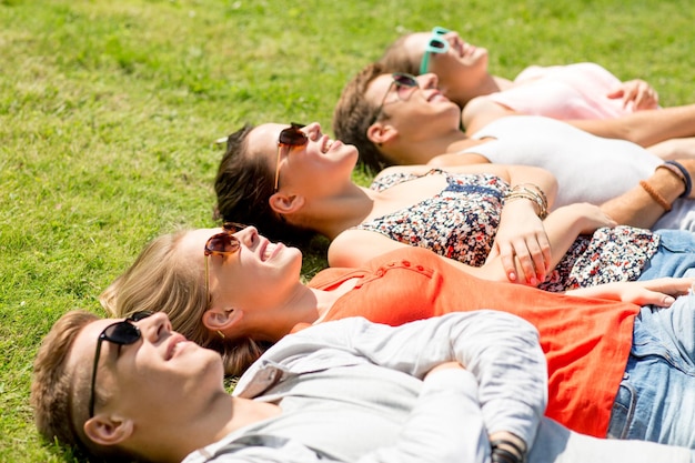 koncepcja przyjaźni, wypoczynku, lata i ludzi - grupa uśmiechniętych przyjaciół leżących na trawie na świeżym powietrzu