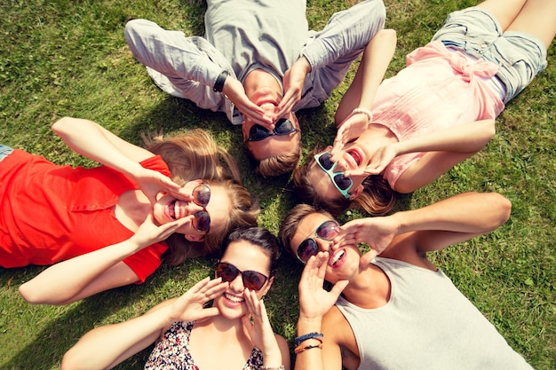 Zdjęcie koncepcja przyjaźni, wypoczynku, lata i ludzi - grupa uśmiechniętych przyjaciół leżących na trawie w kręgu na zewnątrz