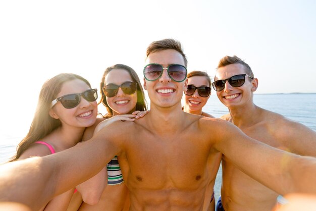 koncepcja przyjaźni, wypoczynku, lata, technologii i ludzi - grupa uśmiechniętych przyjaciół robi selfie na plaży