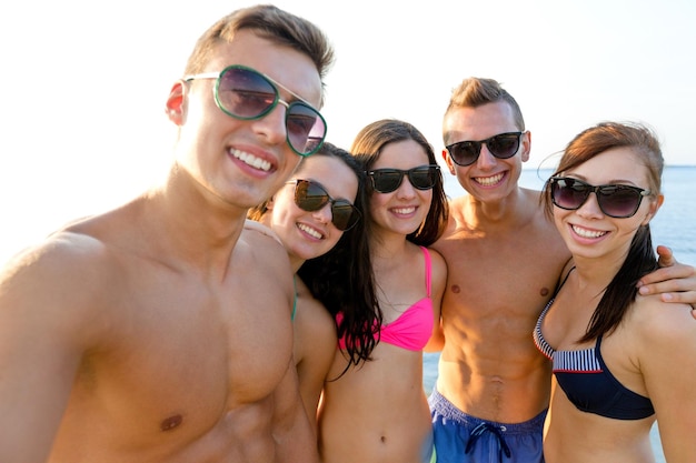 koncepcja przyjaźni, wypoczynku, lata, technologii i ludzi - grupa uśmiechniętych przyjaciół robi selfie na plaży