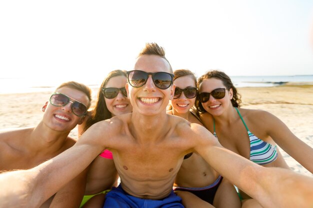 koncepcja przyjaźni, wypoczynku, lata, technologii i ludzi - grupa uśmiechniętych przyjaciół robi selfie na plaży