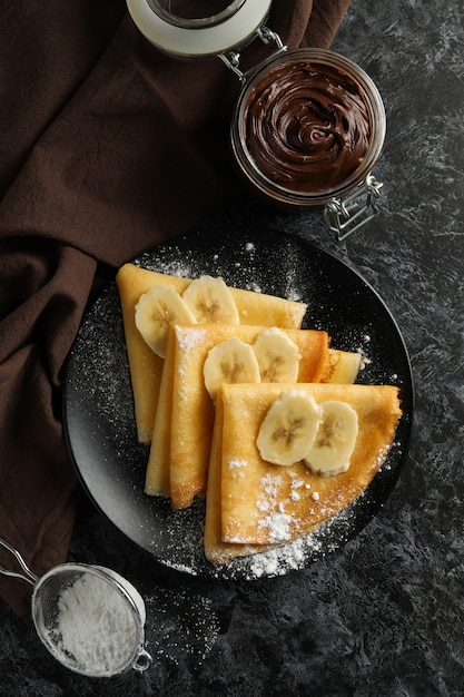 Koncepcja pyszne śniadanie z naleśnikami z cukrem pudrem i bananem na czarnym tle smokey