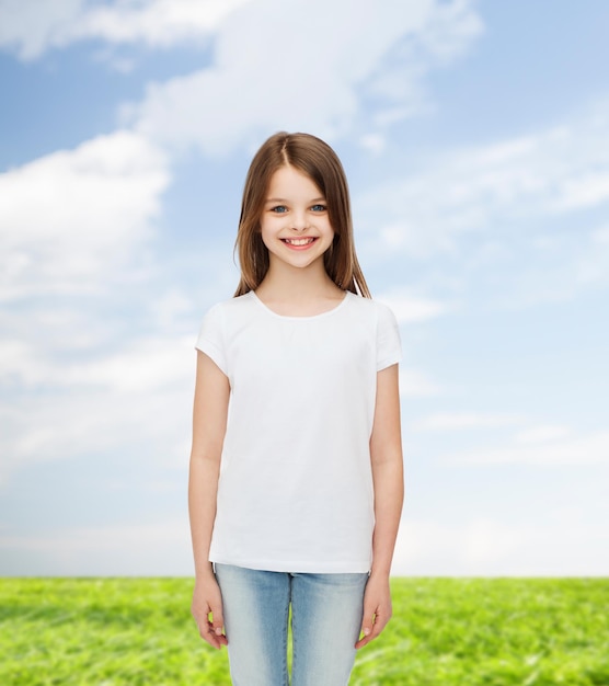 koncepcja reklamy, dzieciństwa, lata i ludzi - uśmiechnięta dziewczynka w białej pustej koszulce trzymająca się nad naturalnym tłem