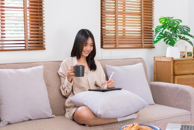 Koncepcja relaksu w domu Azjatka pisze i pracuje na tablecie podczas picia kawy