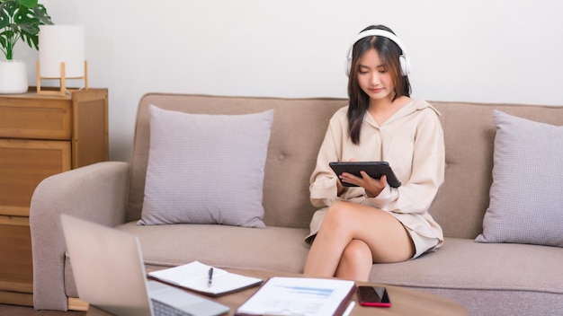Koncepcja relaksu w domu Młoda Azjatycka kobieta słucha muzyki i surfuje w mediach społecznościowych na tablecie