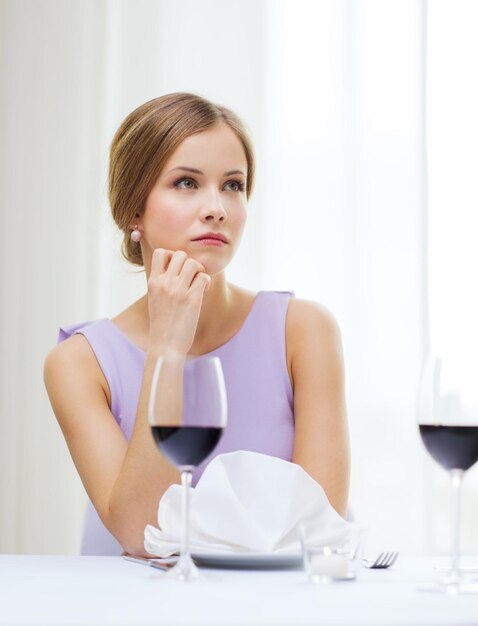 koncepcja restauracji i szczęścia - zdenerwowana młoda kobieta ze szklanką czerwonego skomlenia czekająca na randkę w restauracji