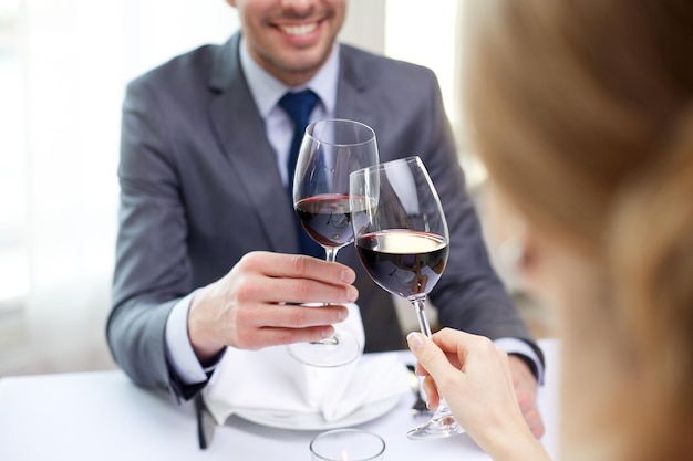 koncepcja restauracji, ludzi, uroczystości i wakacji - zbliżenie młodej pary z kieliszkami czerwonego wina, patrząc na siebie w restauracji