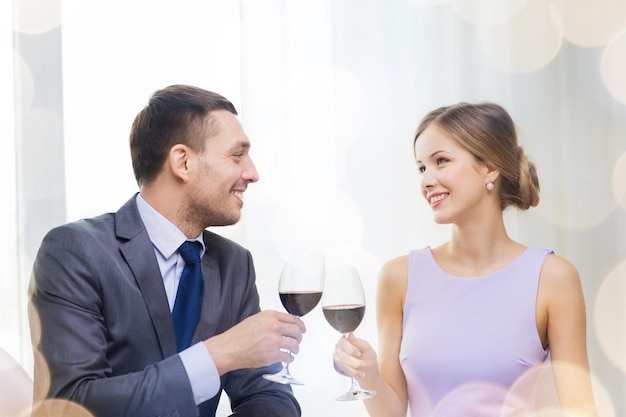 koncepcja restauracji, pary i wakacji - uśmiechnięta młoda para z kieliszkami czerwonego wina patrząca na siebie w restauracji