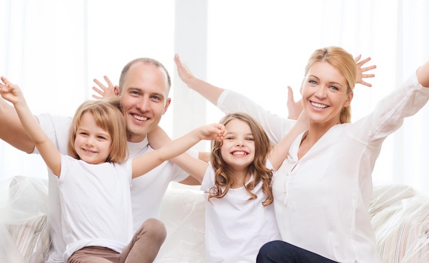 Zdjęcie koncepcja rodziny, dzieci i domu - uśmiechnięci rodzice i dwie małe dziewczynki w domu machające rękami