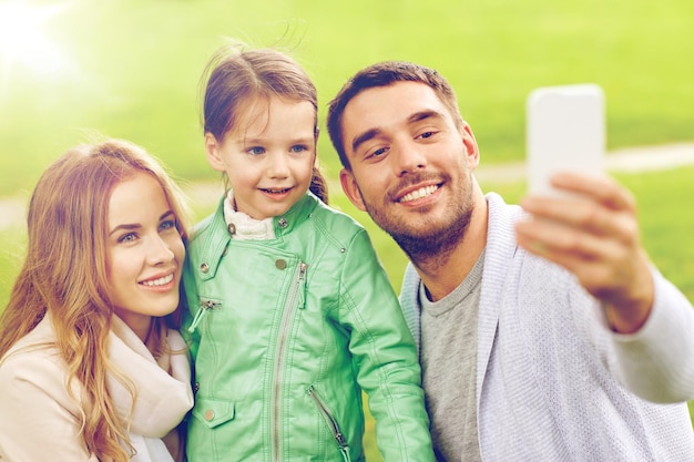 koncepcja rodziny, dzieciństwa, technologii i ludzi - szczęśliwy ojciec, matka i mała córka robią sobie selfie przez smartfon w parku