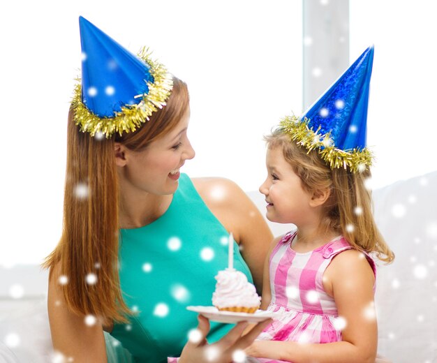 koncepcja rodziny, dzieciństwa, wakacji i ludzi - szczęśliwa matka i córka w niebieskich czapkach imprezowych z ciastem i świeczką