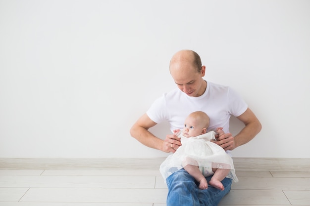 Koncepcja rodziny, ojcostwa i dzieci - łysy ojciec trzyma ładny noworodka w domu na białej ścianie z miejsca na kopię