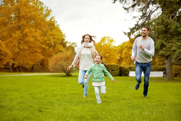 Zdjęcie koncepcja rodziny, rodzicielstwa, wypoczynku i ludzi - szczęśliwa matka, ojciec i mała dziewczynka biegająca i grająca w łapanie w jesiennym parku miejskim