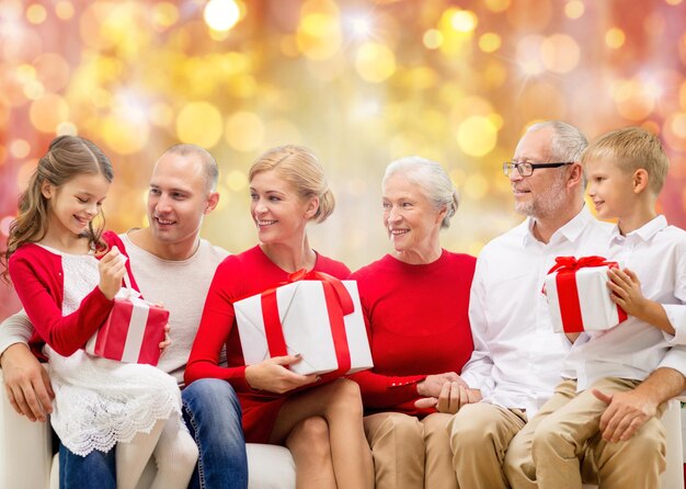 koncepcja rodziny, wakacji, generacji, świąt Bożego Narodzenia i ludzi - szczęśliwa rodzina z pudełkami na prezenty siedzi na kanapie na tle światła