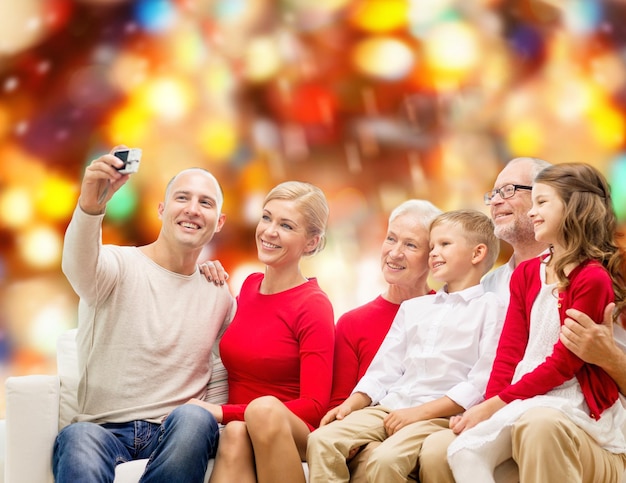 koncepcja rodziny, wakacji, pokolenia, świąt i ludzi - uśmiechnięta rodzina z aparatem robi selfie i siedzi na kanapie nad czerwonym światłem w tle
