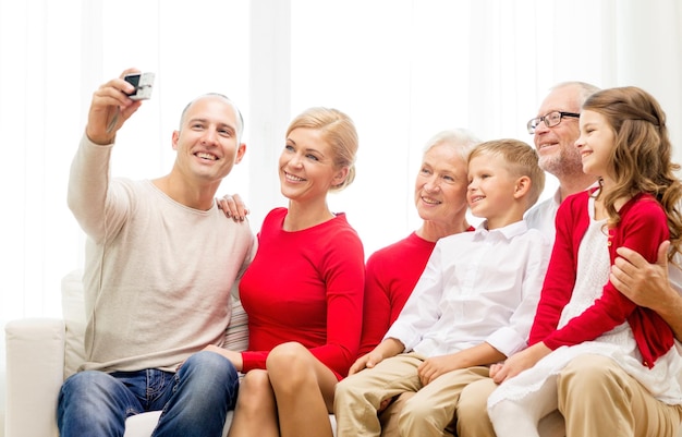 koncepcja rodziny, wakacji, pokolenia, świąt i ludzi - uśmiechnięta rodzina z aparatem robi selfie i siedzi na kanapie w domu