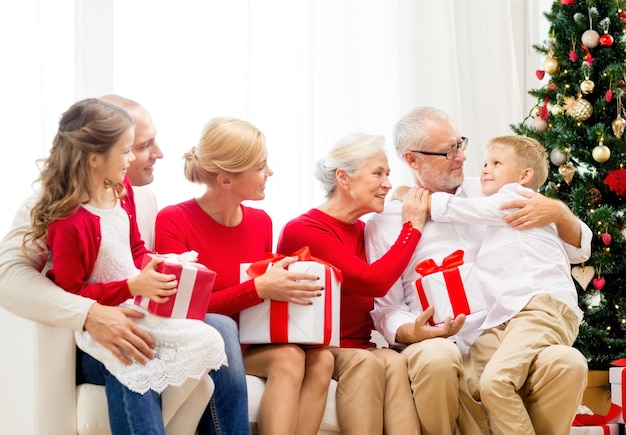koncepcja rodziny, wakacji, pokolenia, świąt i ludzi - uśmiechnięta rodzina z pudełkami na prezenty siedząca na kanapie w domu