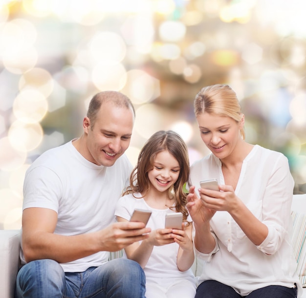 koncepcja rodziny, wakacji, technologii i ludzi - uśmiechnięta matka, ojciec i mała dziewczynka ze smartfonami na tle światła