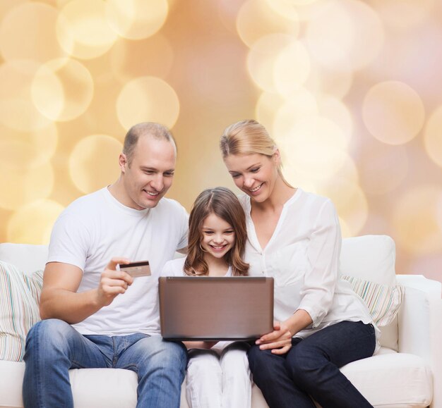 Zdjęcie koncepcja rodziny, wakacji, zakupów, technologii i ludzi - szczęśliwa rodzina z laptopem i kartą kredytową na beżowym tle światła