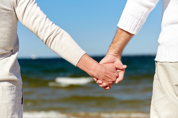koncepcja rodziny, wieku, podróży, turystyki i ludzi - zbliżenie starszej pary trzymającej się za ręce na letniej plaży