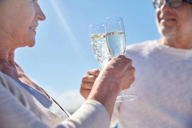koncepcja rodziny, wieku, wakacji, wypoczynku i ludzi - zbliżenie szczęśliwej pary seniorów brzęczące kieliszki do szampana na letniej plaży