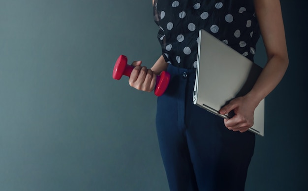 Koncepcja równowagi życia zawodowego, prezentowana przez Biznesową kobietę pracującą trzymającą laptop i hantle, styl życia współczesnych ludzi. Skadrowany obraz z miejsca kopiowania