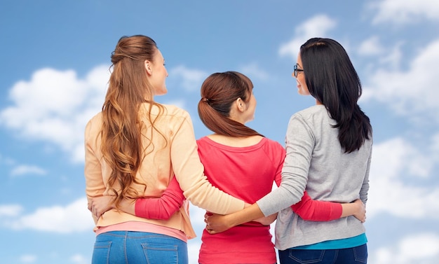 Zdjęcie koncepcja różnorodności, przyjaźni i ludzi - międzynarodowa grupa szczęśliwych różnych kobiet przytulających się od tyłu na tle błękitnego nieba i chmur