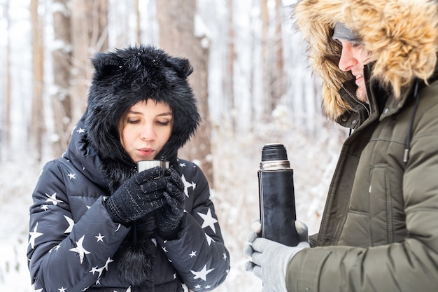 Koncepcja sezonu i spaceru - szczęśliwa para pijąca gorącą herbatę w zimowym lesie