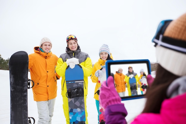 Zdjęcie koncepcja sportów zimowych, technologii, wypoczynku, przyjaźni i ludzi - szczęśliwi przyjaciele ze snowboardami i komputerem typu tablet, robiący zdjęcia na zewnątrz