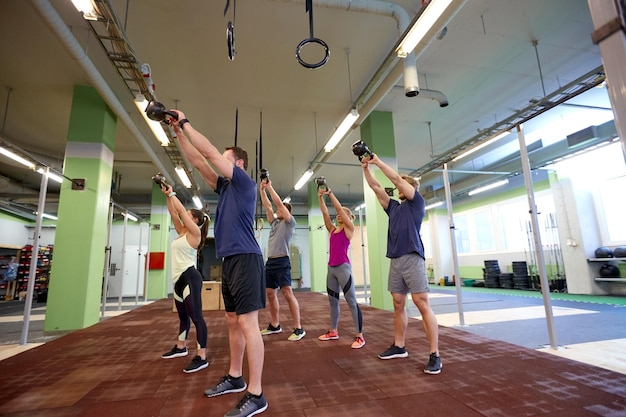 koncepcja sportu, fitness, podnoszenia ciężarów i treningu - grupa osób z kettlebellami i urządzeniami do śledzenia tętna ćwiczących na siłowni