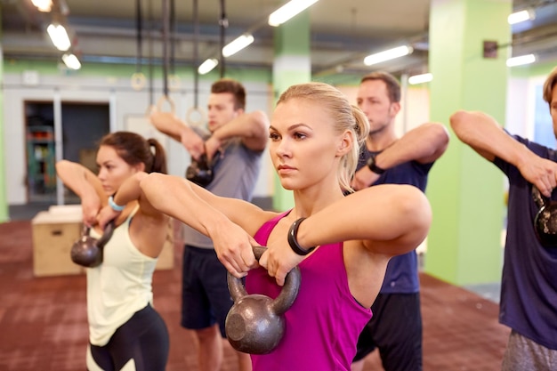 koncepcja sportu, fitness, podnoszenia ciężarów i treningu - grupa osób z kettlebellami i urządzeniami do śledzenia tętna ćwiczących na siłowni