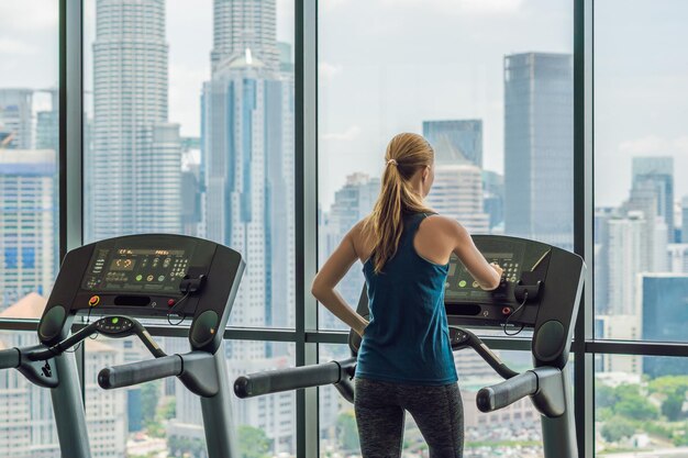 Koncepcja sportu, fitness, stylu życia, technologii i ludzi - kobieta ćwicząca na bieżni w siłowni na tle wielkiego miasta