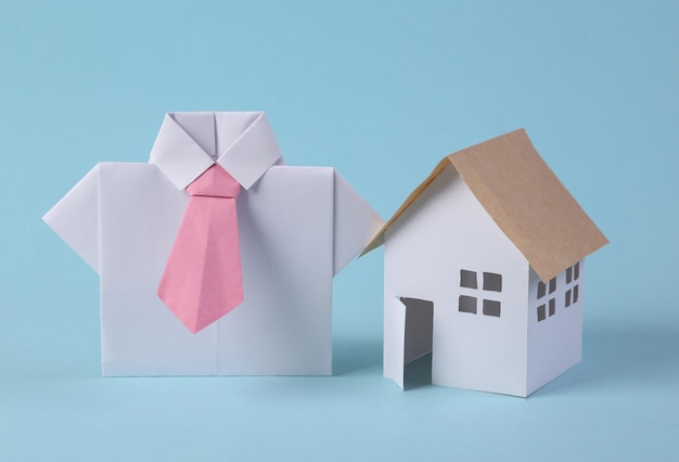 Koncepcja sprzedaży domu Realtor origami koszula i figurka domu na niebieskim tle