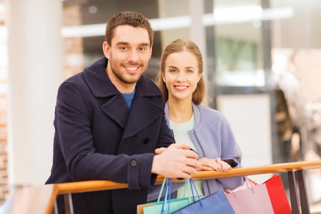 koncepcja sprzedaży, konsumpcjonizmu i ludzi - szczęśliwa młoda para z torbami na zakupy w centrum handlowym